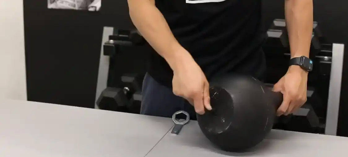 Bells of steel adjustable kettlebell close up using tool to unscrew bottom of kettlebell on table.